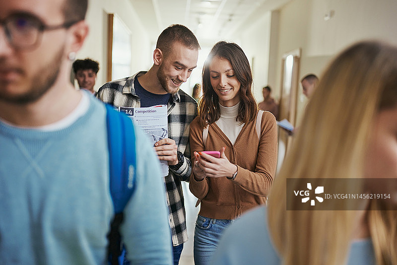 幸福的大学情侣在走廊里用手机。图片素材