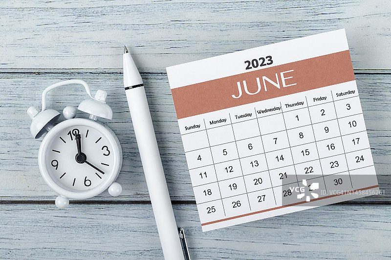 日历桌2023:六月是组织者在木桌背景上用闹钟和白笔做计划和截止日期的月份。图片素材