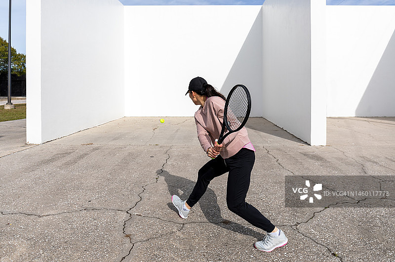 年轻的女运动员对着手球场的墙练习网球图片素材