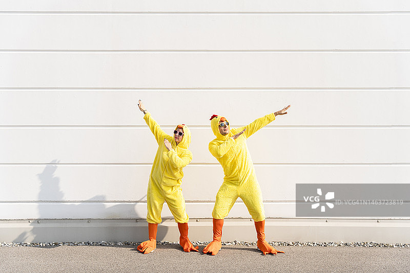 爱玩的男人和女人穿着鸡服装，在墙前玩得很开心图片素材