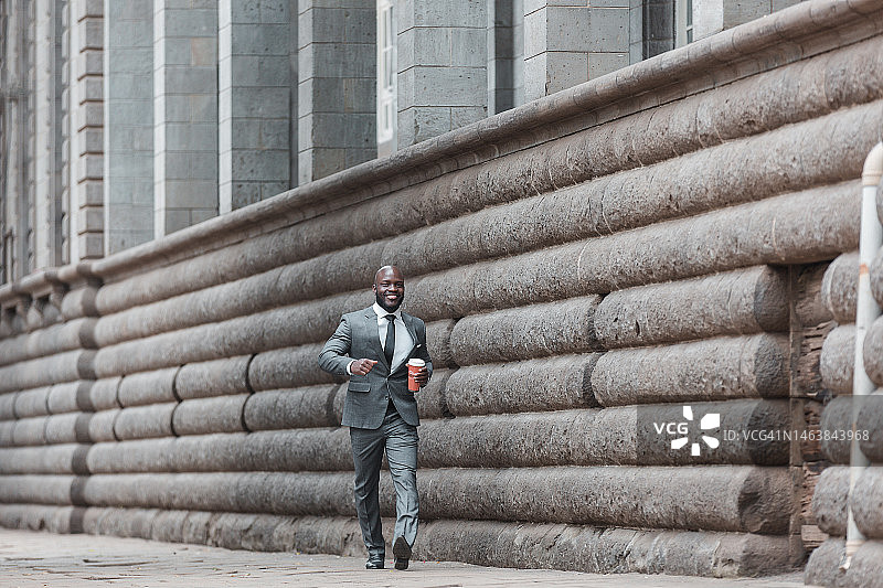 一名男子走在东非肯尼亚内罗毕市的街道上，手里拿着一杯塑料茶图片素材