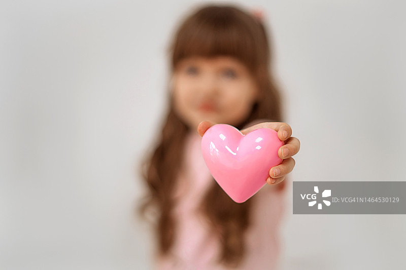 可爱的小女孩手里拿着一颗粉红色的心站在白色的沙滩上图片素材