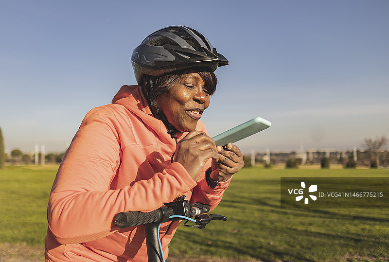 快乐的高级妇女推踏板车使用扬声器电话在阳光灿烂的日子图片素材