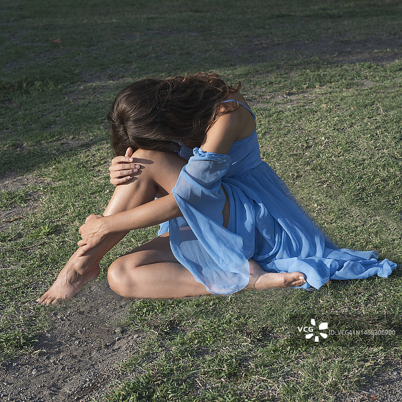 意大利拉齐奥，特维尼亚诺罗马诺，一名穿着夏装的赤脚女子坐在草地上图片素材