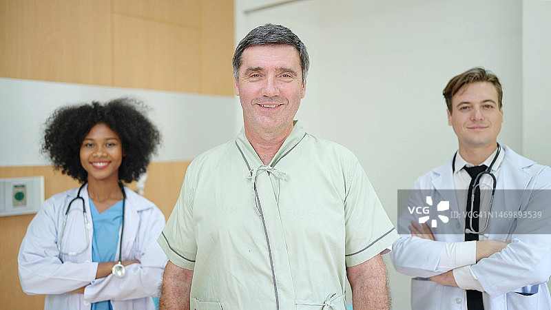 微笑着接受治疗的病人看着镜头，一组医疗多样性团队站在病房后面。长者保健概念图片素材