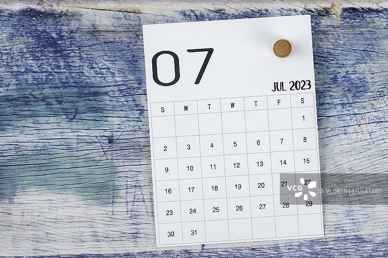 2023日历台:七月是组织者计划和截止日期的月份，蓝色木制背景上有一个图钉。图片素材