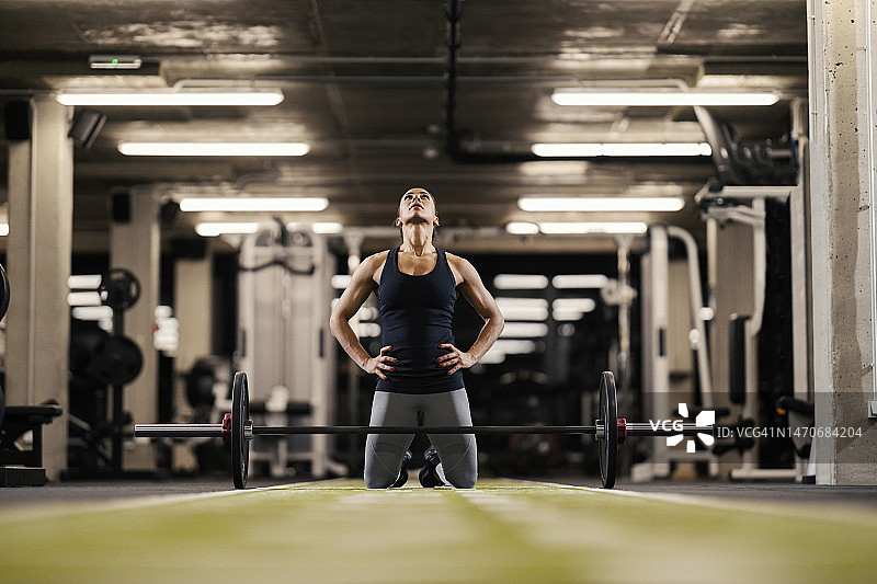 在健身房里，一名女健身运动员跪在地上，正准备举杠铃。图片素材