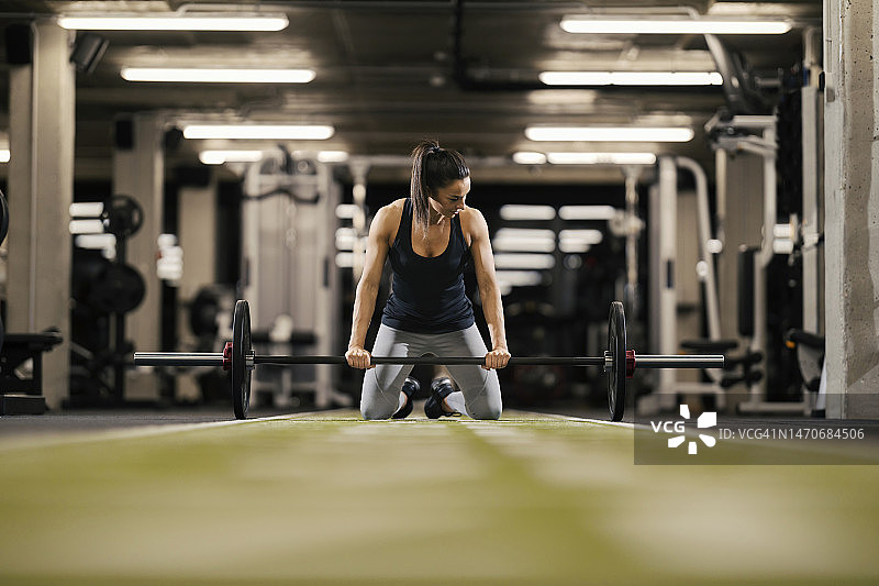 一位身材健美的女健身运动员正在健身房准备举杠铃。图片素材