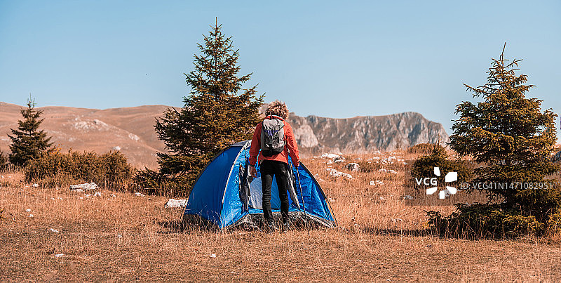 带着帐篷的一名男子一边在山上露营，一边用智能手机享受阳光图片素材