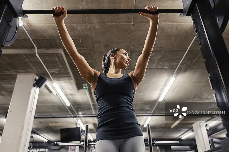 一个肌肉发达的女运动员斜靠在杠铃上，在健身房看向别处。图片素材