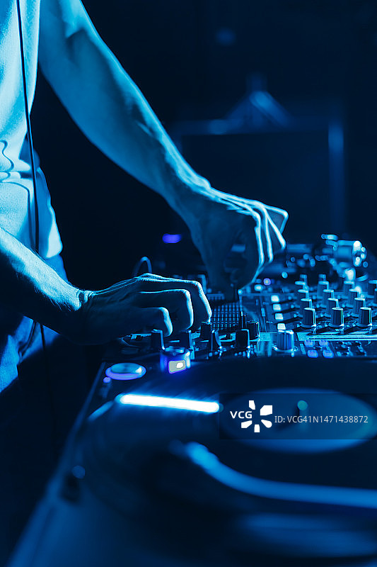 俱乐部DJ在蓝色舞台灯光下混音黑胶唱片。近距离的照片，唱片骑师播放音乐的派对在夜总会图片素材