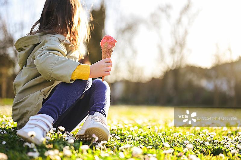 一个不认识的孩子坐在春天的草坪上，吃着草莓冰淇淋。副本的空间。图片素材