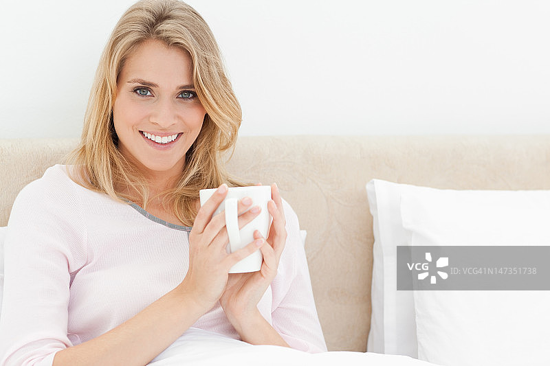 女人坐在床上，手里拿着一个杯子，微笑着向前看图片素材
