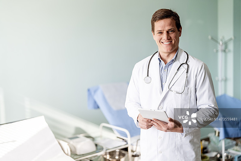 微笑的年轻医生站在他的办公室和使用数字平板电脑图片素材