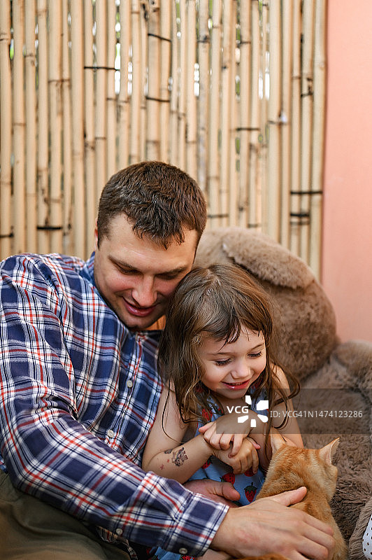 坦诚的时刻。一个女孩和一只猫的友谊。可爱的肖像猫和孩子与爸爸拥抱。可爱的小蹒跚学步的女孩玩她的家畜宠物图片素材