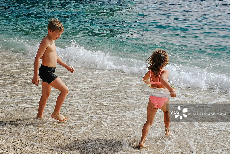 两个孩子在岸边玩耍，在海里游泳。假期的概念，旅行，度假。夏天在土耳其克利奥帕特拉海滩的孩子们。图片素材