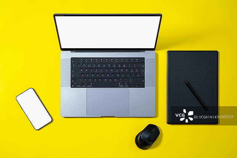 商务工作空间平铺。现代笔记本电脑，手机与空白的白色屏幕和电脑鼠标在黄色背景。高角视图。图片素材