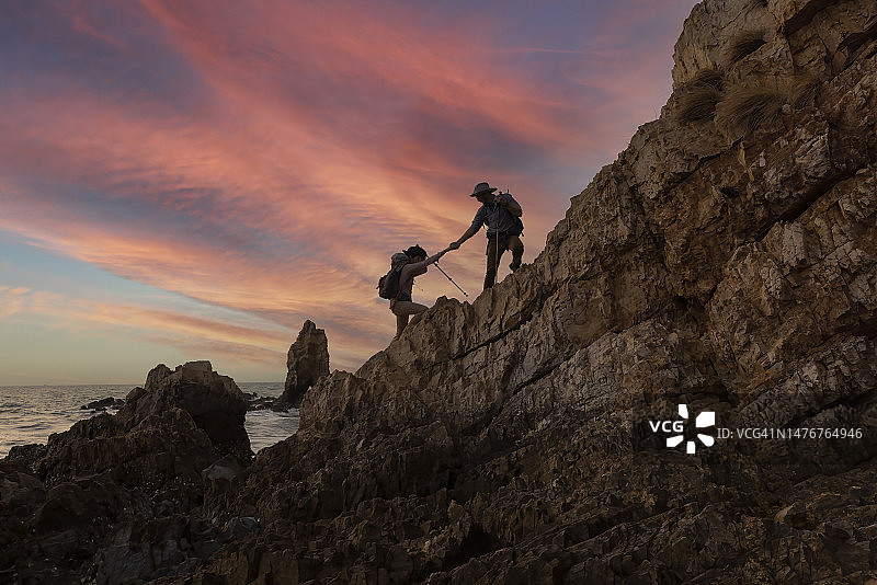 徒步队员手牵手，互相帮助，同时爬上岩石山的冒险旅行概念图片素材