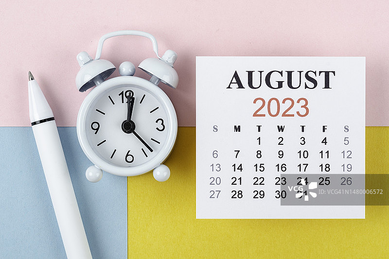 日历桌2023:8月是组织者用闹钟和白笔在双色纸背景下计划和截止日期的月份。图片素材