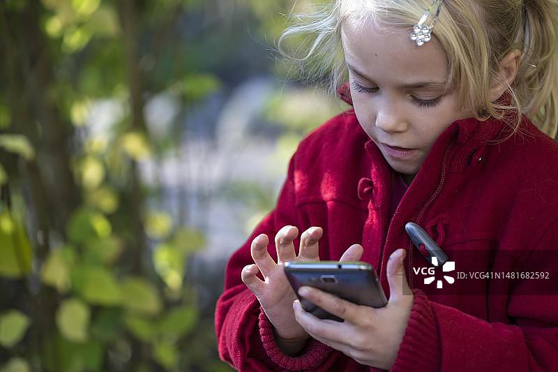 德国石勒苏益格-荷尔斯泰因州基尔市，带智能手机的女孩(7岁)图片素材