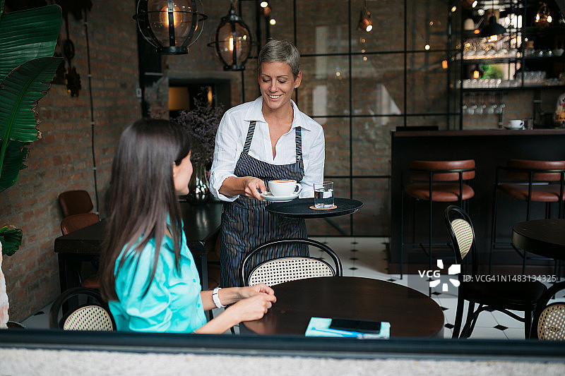 在咖啡馆给女商人端咖啡的女服务员图片素材