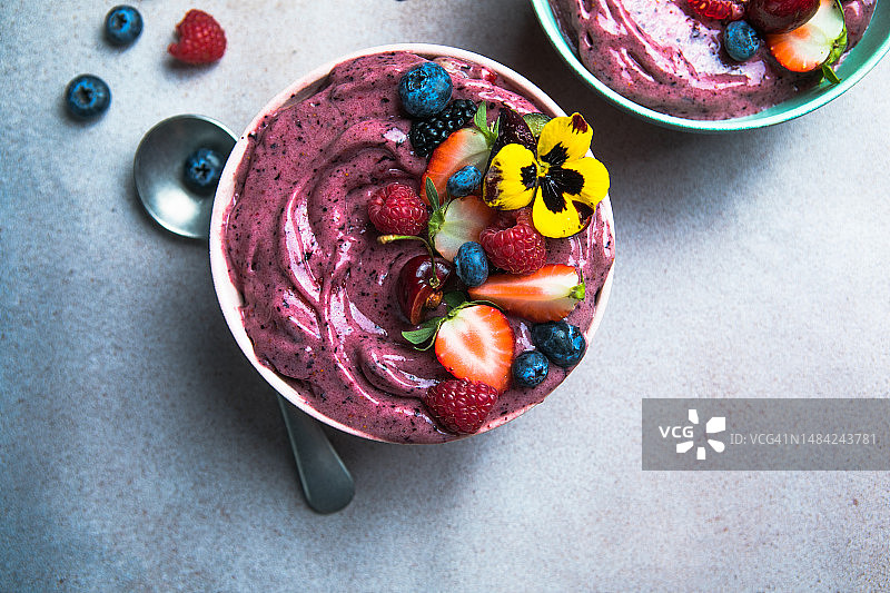 两碗夏日巴西莓奶昔配上草莓，蓝莓，灰色混凝土背景。早餐碗与水果和谷物，特写，俯视图，健康食品图片素材