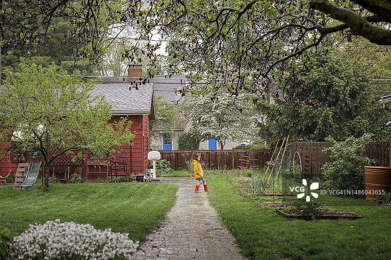 远处的孩子穿着靴子在后院的雨中玩耍图片素材