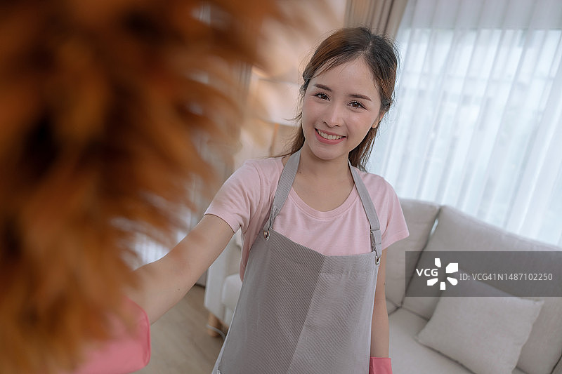 年轻的亚洲女人在假期的空闲时间打扫家里的客厅。图片素材