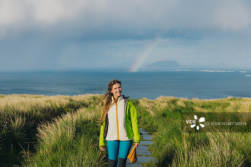 一个快乐的女人在挪威海上美丽的彩虹下徒步旅行图片素材