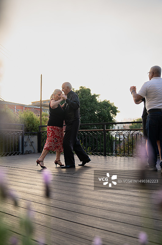 老夫妇在露台上优雅地跳舞的垂直照片，周围是模糊的花朵图片素材