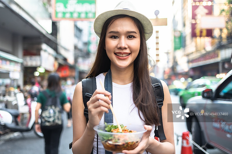年轻的成年亚洲吃货女背包旅行者在唐人街街头小吃吃亚洲甜点。旅游女孩们正在享受曼谷美丽的地方。图片素材