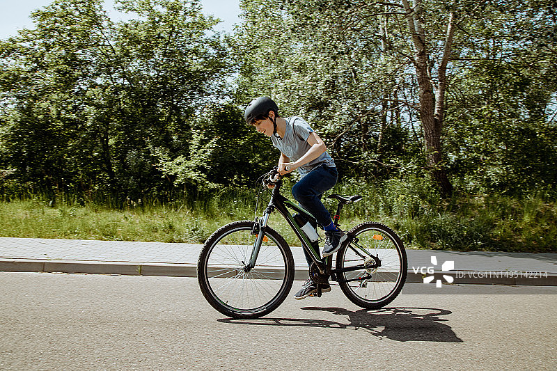 爱冒险的少年穿着运动服，戴着安全帽在公路上骑自行车图片素材