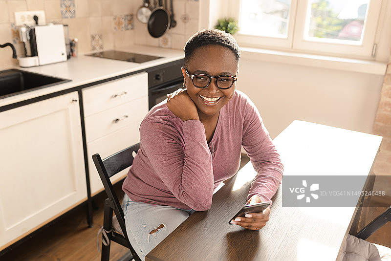 一个快乐的非洲年轻女子在家里使用智能手机的肖像图片素材