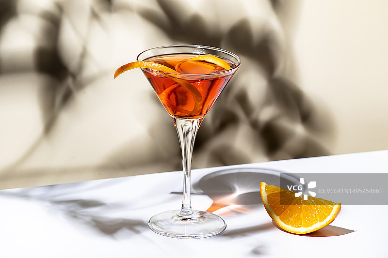 马丁内斯橙味鸡尾酒，以红色苦艾酒、利口酒、苦味、柑橘皮和冰块混合而成。浅米色背景，硬光，阴影图案图片素材