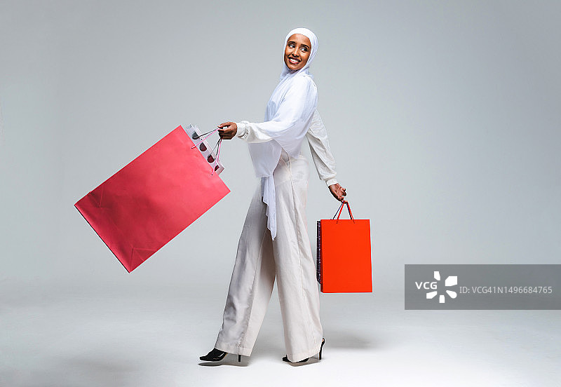 阿拉伯联合酋长国，一个微笑的女人拿着购物袋站在灰色的背景下图片素材