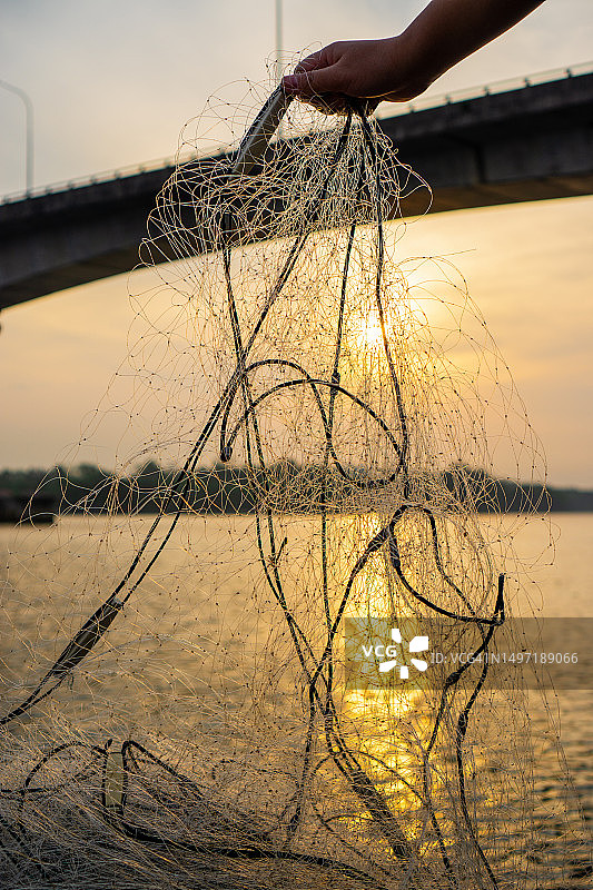 手拿渔网对着水面在日出图片素材