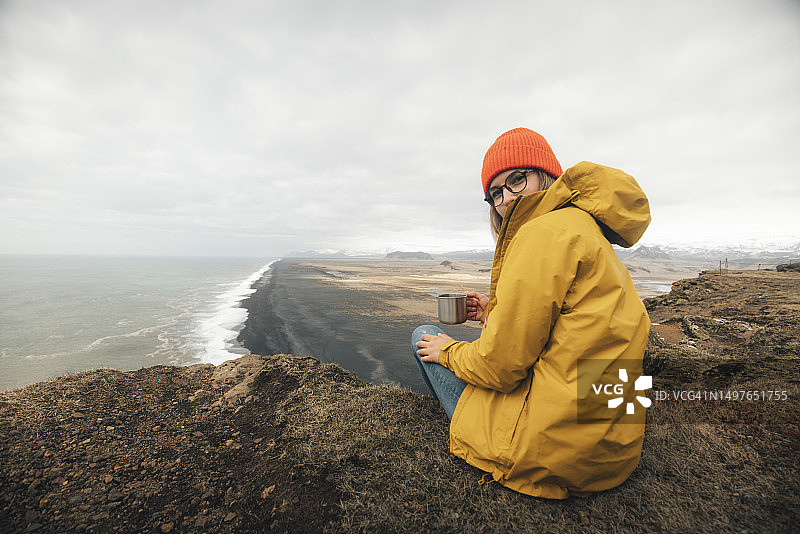 一个女人坐在海角上享受大自然的画像。冰岛图片素材