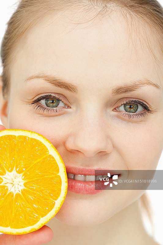 一个女人把一个橙子放在她的嘴唇上的特写图片素材