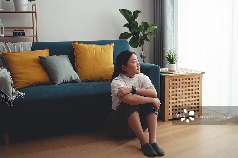 一个亚洲女人坐在家里，抱着膝盖思考着孤独的问题。图片素材