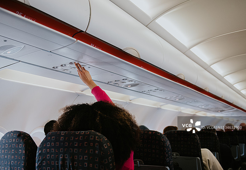 在一架商用飞机上，一名女子伸手去调节她指定座位上方的空调。图片素材