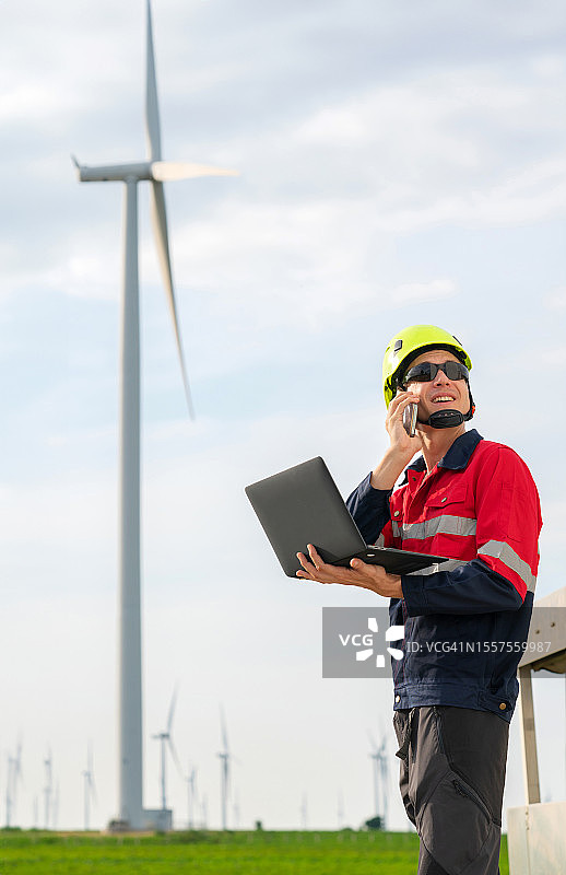 在一个巨大的风力涡轮机农场工作的机械工程师使用笔记本电脑监控关键参数并查看风力涡轮机。专注分析数据以确保最佳性能和能量生成。图片素材