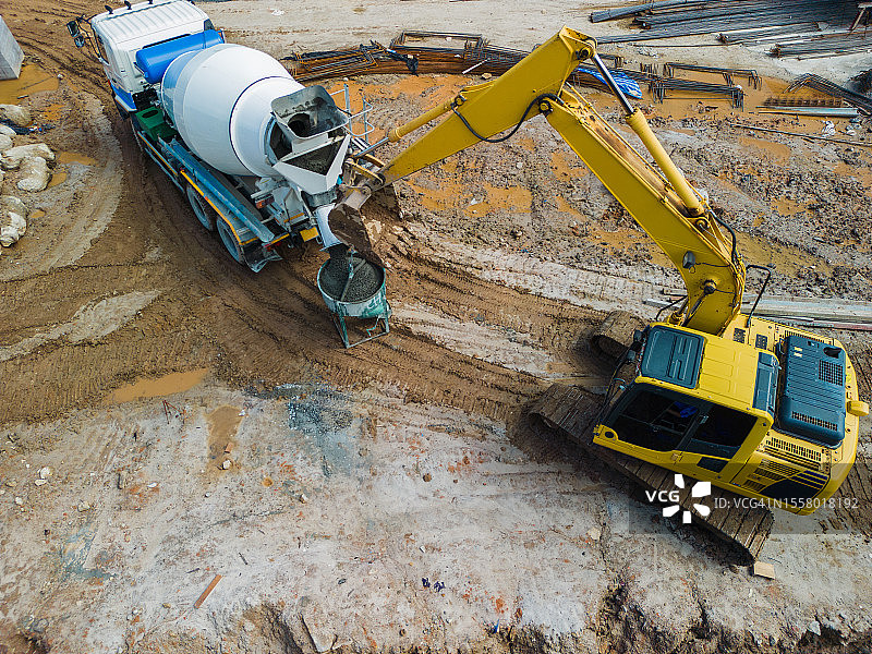 鸟瞰图施工现场，挖掘机正在帮忙吊起混凝土搅拌机，供混凝土运输车将混凝土倒入朋友们的结构中使用。图片素材