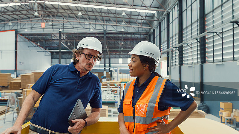 专业男性工业工程师在制造工厂使用平板电脑时与工厂工人交谈。在制造厂或生产厂工作。图片素材