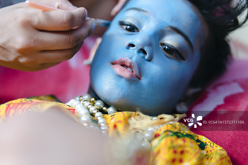 一个印度小男孩把自己的脸涂成蓝色，就像主奎师那一样。图片素材