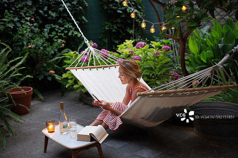 一个女人在花园的吊床上放松，看着智能手机图片素材