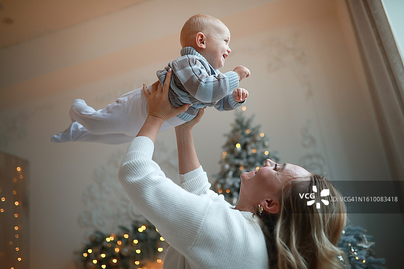 温馨的时刻:母亲抱着微笑的蹒跚学步的儿子，圣诞装饰图片素材