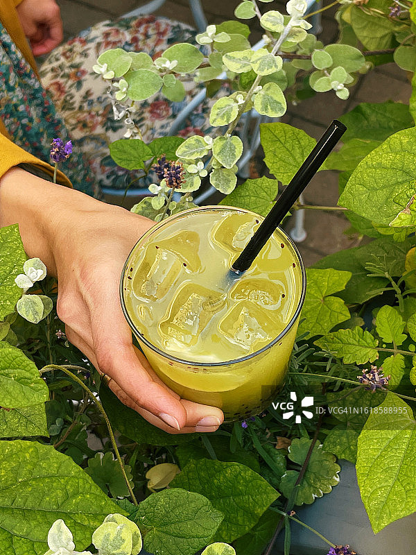 一个女人站在户外，拿着一杯绿色的猕猴桃和罗勒混合的鸡尾酒图片素材