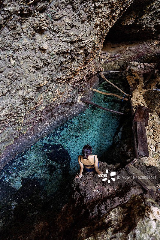 美丽的亚洲女人坐在岩石附近的天然泉水清澈的蓝色的水图片素材
