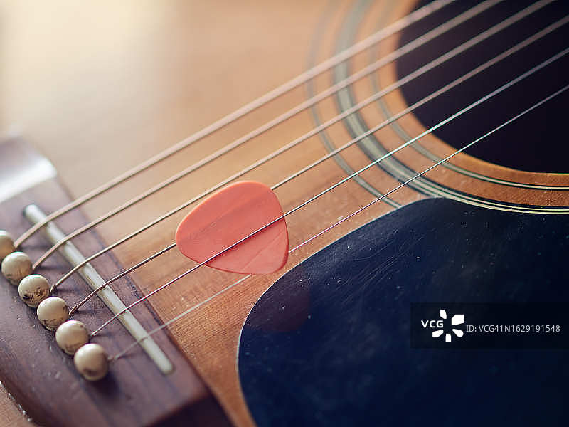 原声吉他的特写，弦上有一个橙色的吉他拨片图片素材