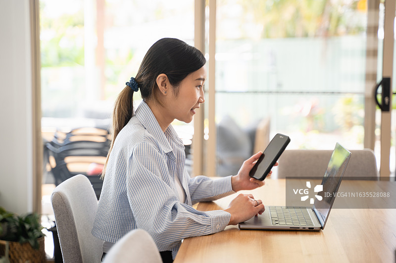 年轻的成年亚洲女商人使用笔记本电脑进行在线会议，同时与她的同事在家里办公室交谈和讨论图片素材